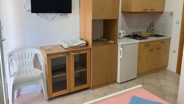 Eine kompakte Küche mit Holzschränken, einem kleinen Kühlschrank, einem Herd und einem an der Wand befestigten Fernseher.