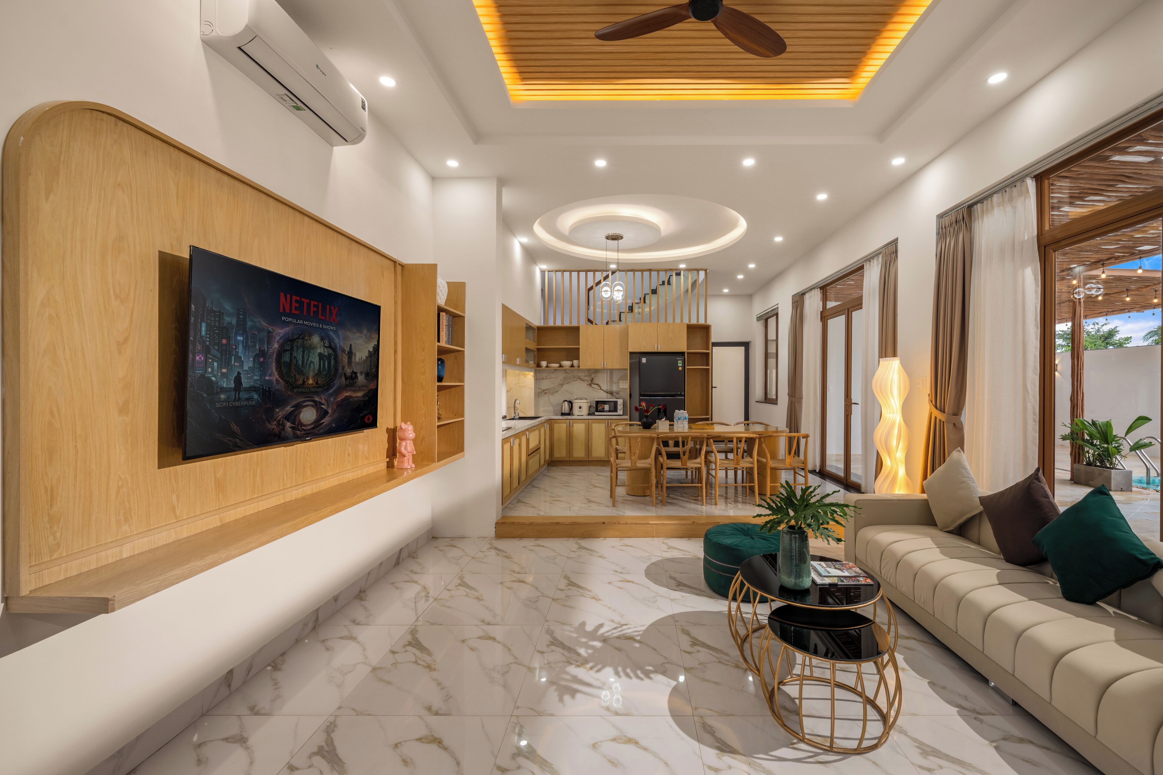 A modern living room with a flat-screen TV, a sofa, a dining area, and a kitchen.