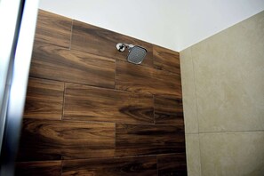 Una ducha con pared de paneles de madera y pared con azulejos color beige.