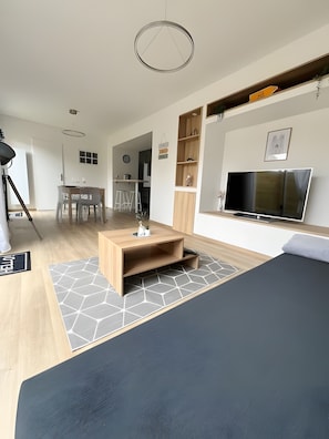 Une chambre dâhĂŽtel moderne avec un lit, une tĂ©lĂ©vision, une table basse en bois et un coin cuisine Ă lâarriĂšre-plan.