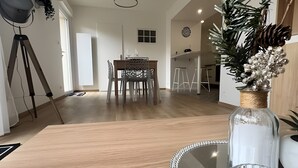 A modern kitchen with a wooden countertop, a glass-top dining table, and a decorative vase with pinecones.