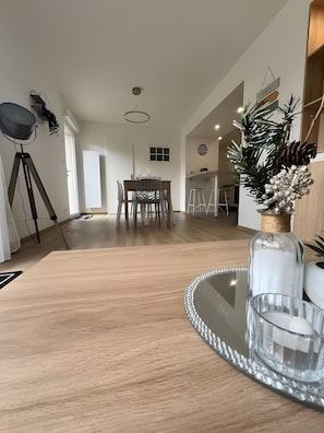 Une cuisine moderne avec un plan de travail en bois, une table à manger à plateau en verre et un vase décoratif contenant des pommes de pin.