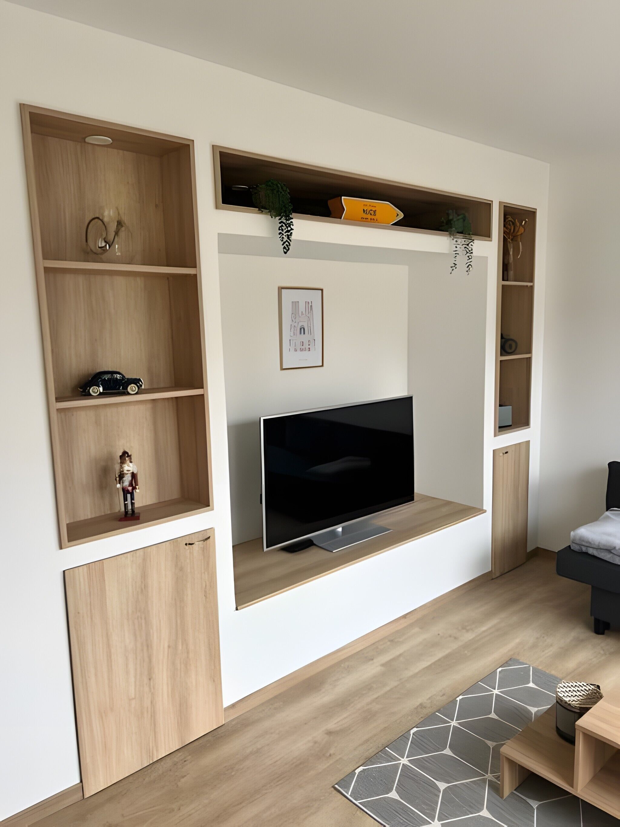 A modern living room with a flat-screen TV, wooden shelving units, and a small cabinet.