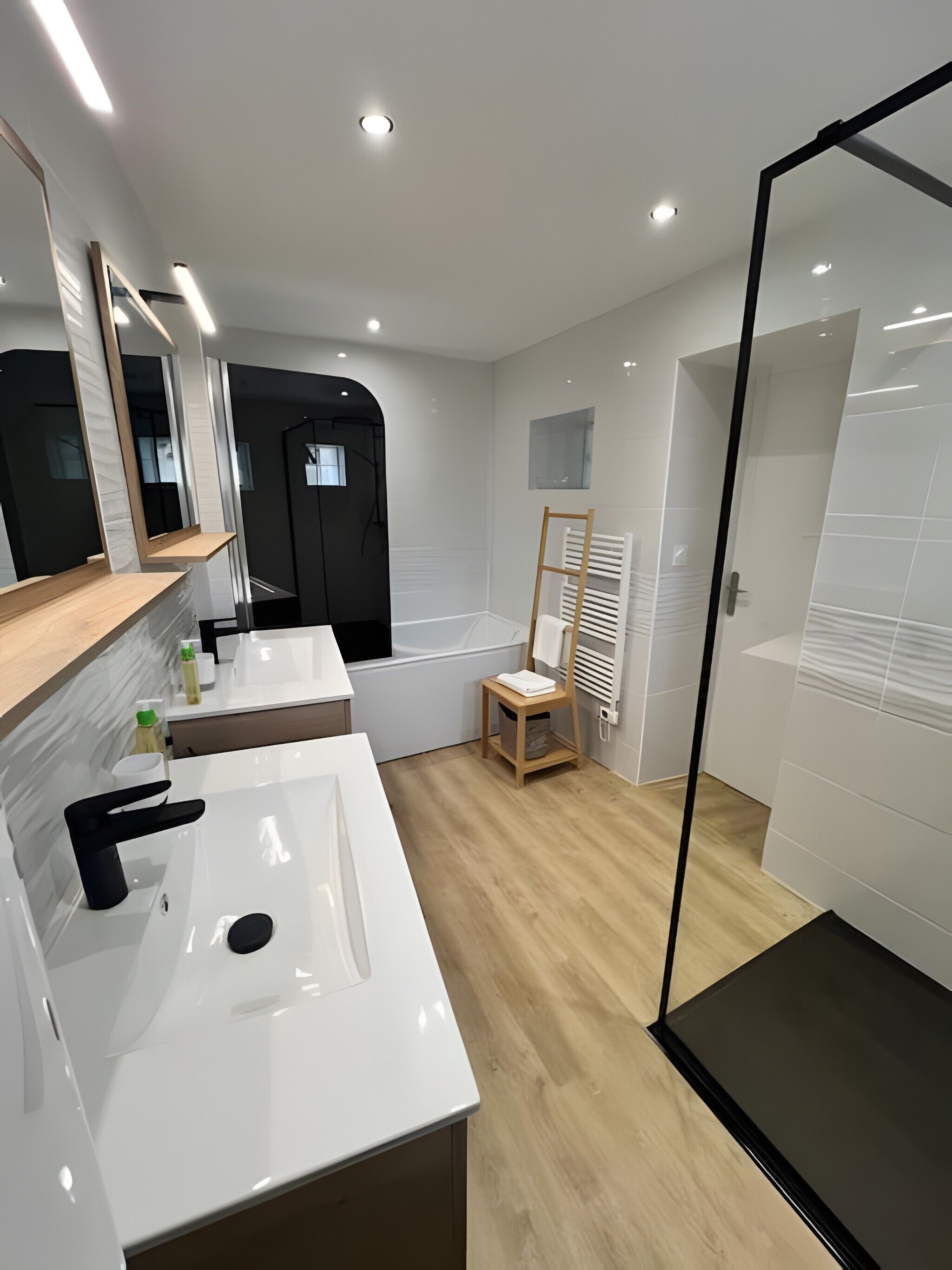A modern bathroom with a white sink, mirror, and bathtub. There is a wooden chair and a towel rack.