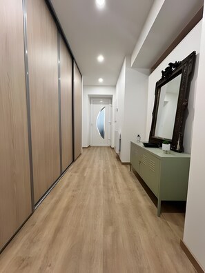 Un couloir dotĂ© dâun plancher en bois, dâun miroir et dâune porte avec un panneau de verre incurvĂ©.