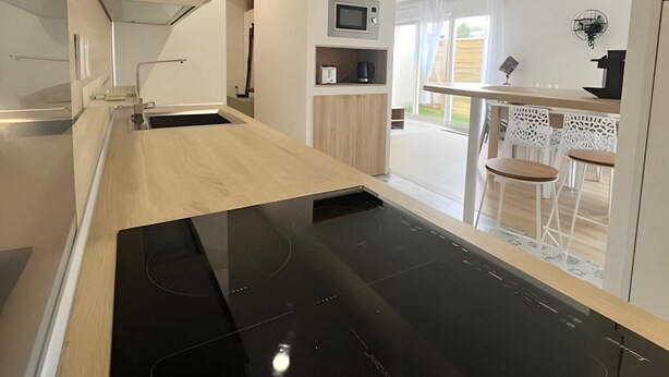 A modern kitchen with a black induction cooktop, wooden countertops, a microwave, and a small dining area with white chairs.