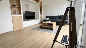 A modern living room with a flat-screen TV, wooden shelving, a sofa, and a tripod-mounted camera.
