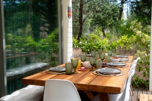 Une table de salle à manger en bois, mise avec des assiettes, des verres et une carafe de jus d’orange, entourée de chaises blanches.