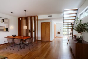 Un intérieur moderne avec une table à manger en bois, des chaises, un mur décoratif et un escalier offrant une vue.