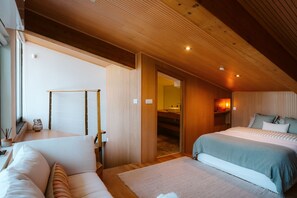 Une chambre avec deux lits, un plafond en bois et une salle de bain visible à travers une porte ouverte.