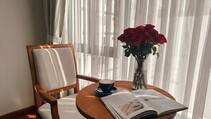 A wooden chair with a cushion, a round wooden table with a book and a cup, and a vase with red roses. - Zesty Hostel & Bistro (Nha Trang)