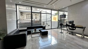 A modern reception area with a reception desk, a black leather sofa, a glass coffee table, and a large window offering a view of the cityscape. - Zesty Hostel & Bistro (Nha Trang)