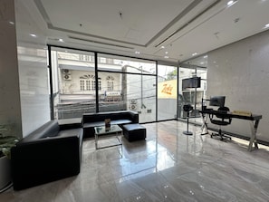 Un área de recepción moderna con mostrador, un sofá de cuero negro, una mesa de centro de vidrio y un amplio ventanal con vistas a la ciudad.