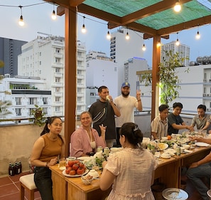 A rooftop dining area with a long table, chairs, and a cityscape view in the background.