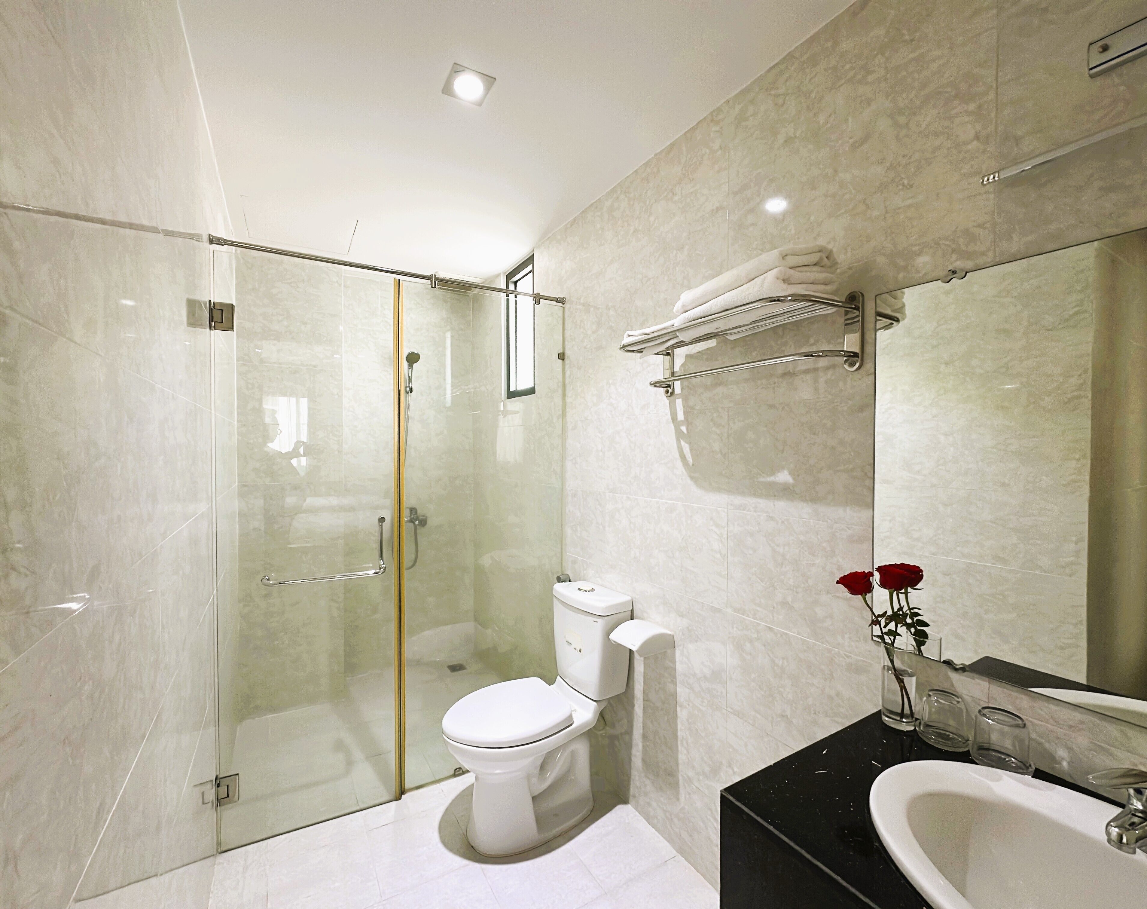 A modern bathroom with a glass-enclosed shower, a white toilet, a black countertop sink, and a mirror with a towel rack.