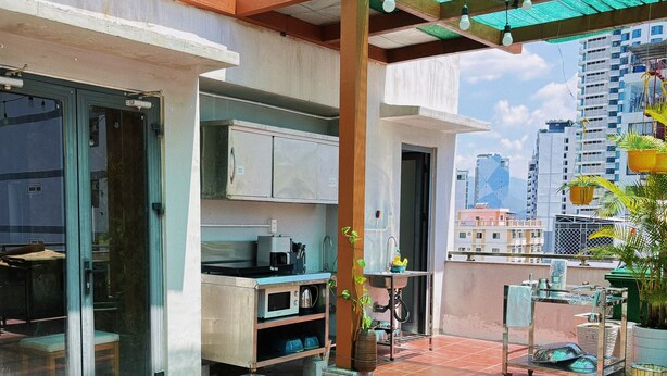 A patio with a wooden table and stools, a kitchen area, and a view of the cityscape. - Zesty Hostel & Bistro (Nha Trang)