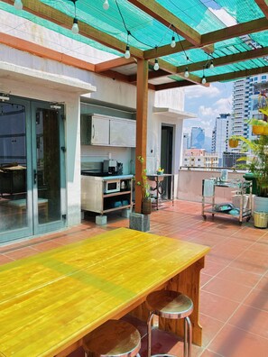 A patio with a wooden table and stools, a kitchen area, and a view of the cityscape. - Zesty Hostel & Bistro (Nha Trang)