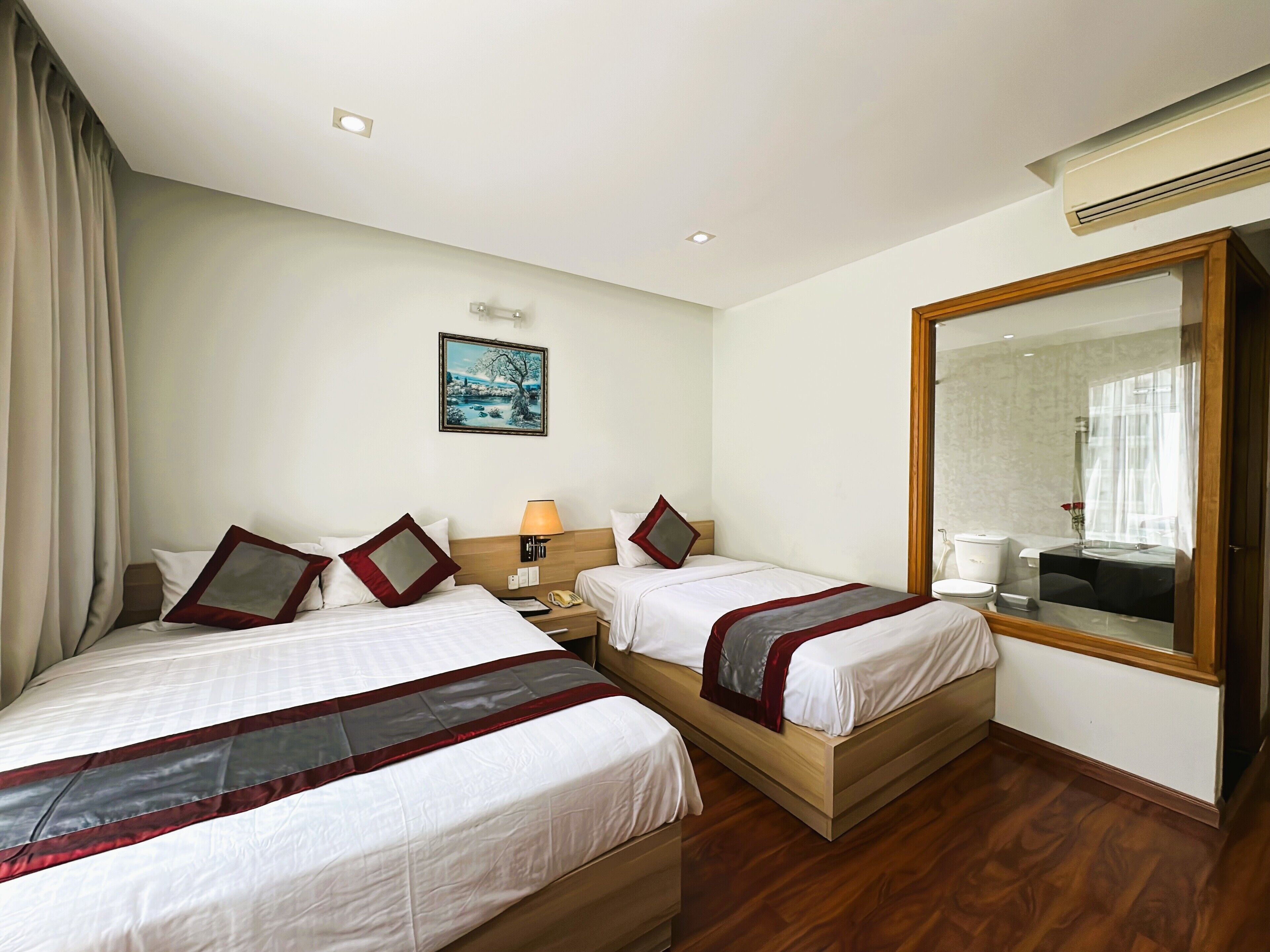 Habitación de hotel con dos camas, una mesita de noche, una lámpara, un cuadro en la pared, un espejo grande y un equipo de aire acondicionado.