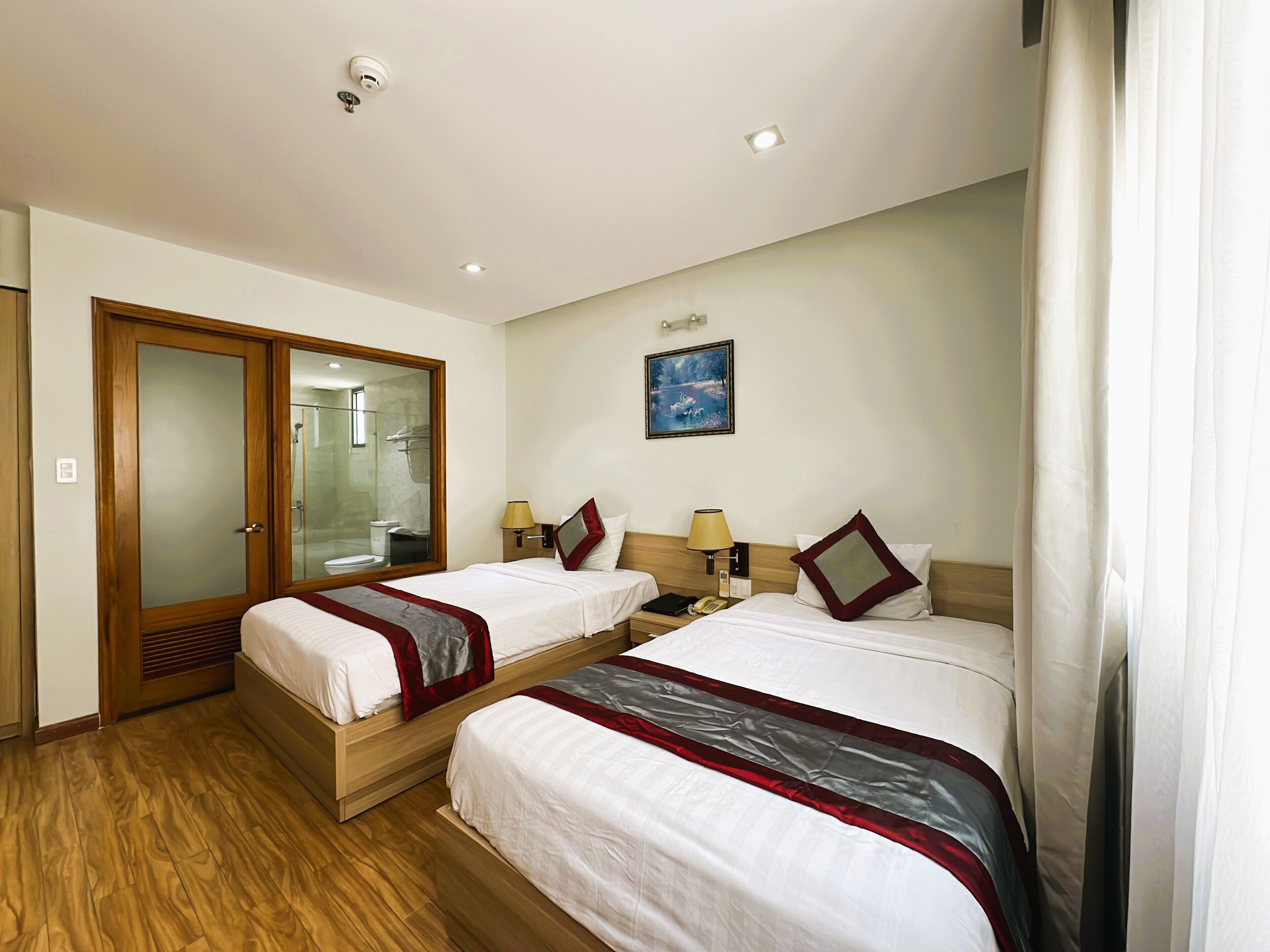 Een hotelkamer met twee bedden, een houten garderobe, een badkamer met een glazen deur en een schilderij aan de muur.