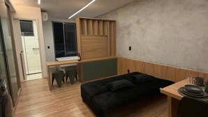 Un appartement moderne avec un plancher en bois, un canapé noir, une table à manger et un coin cuisine.