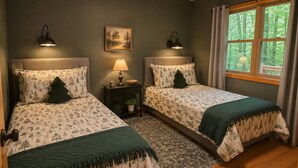 A bedroom with two beds, a nightstand with a lamp, a painting on the wall, and a window with curtains. - Honey Ridge Forest Retreat (Benton Township)