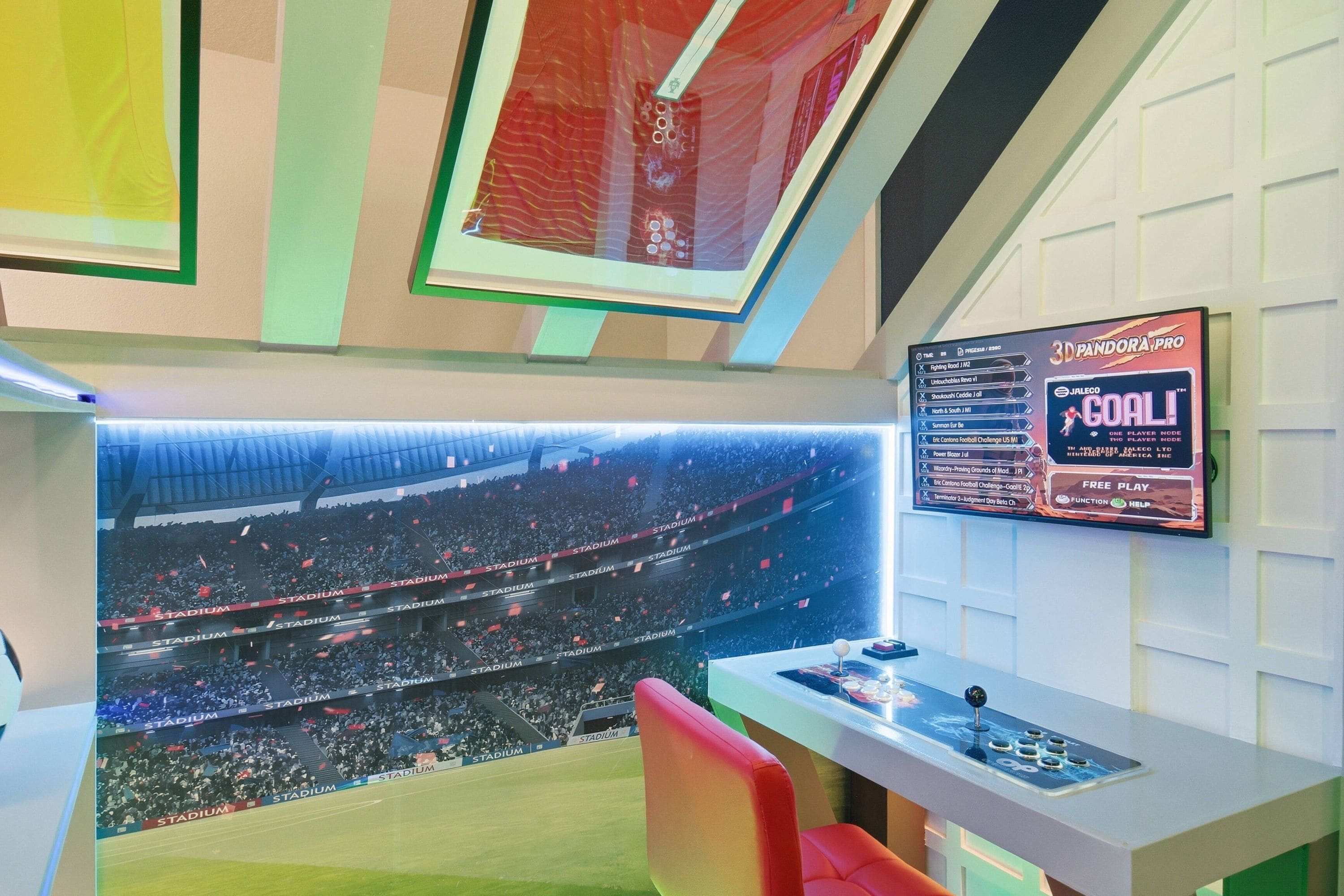 A room with a large screen displaying a stadium view, a 3D gaming console, and a wall-mounted sign.