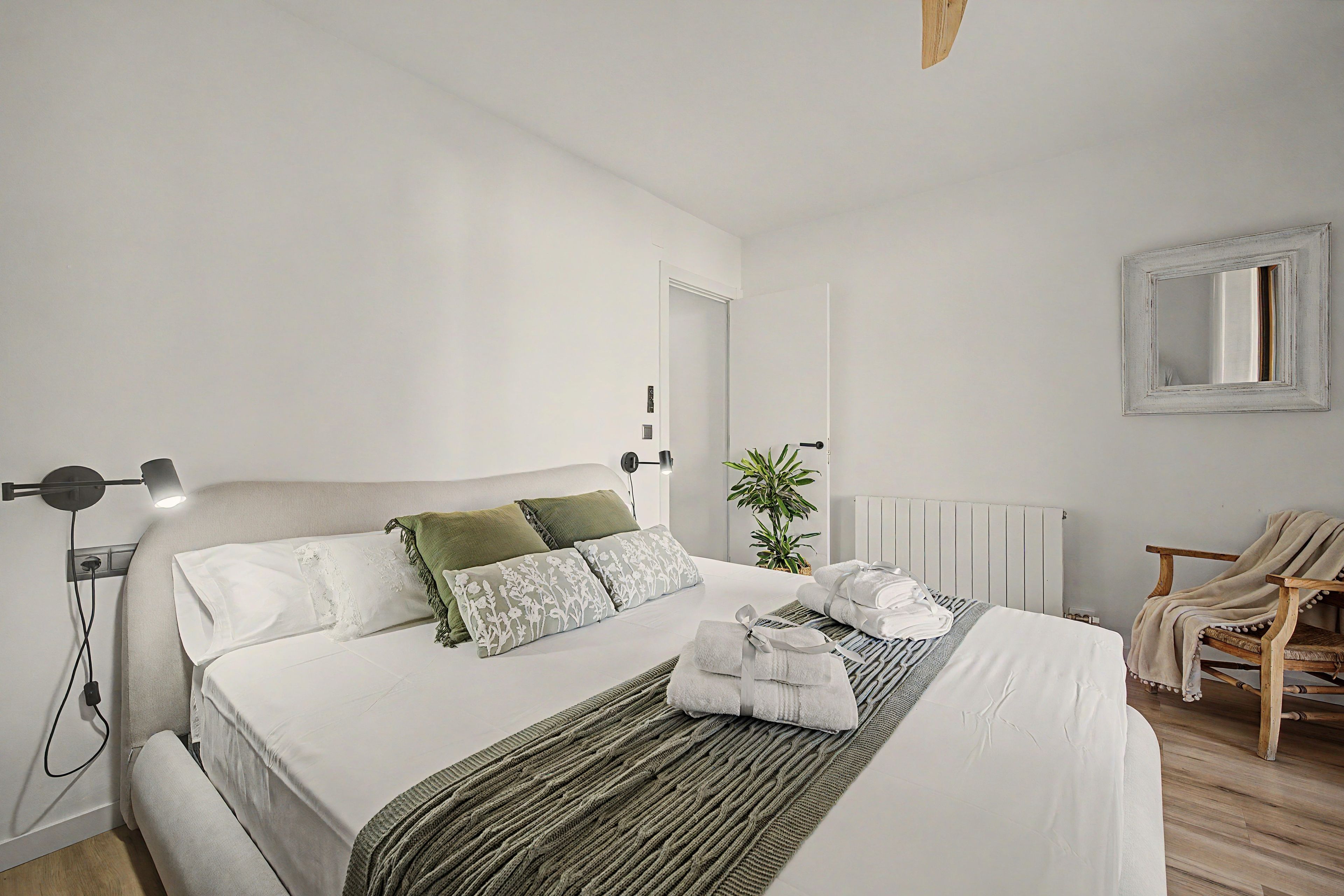 Un dormitorio moderno con cama, lámparas de noche, un radiador, una silla y una planta en maceta.