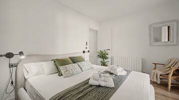 Un dormitorio moderno con cama, lámparas de noche, un radiador, una silla y una planta en maceta.