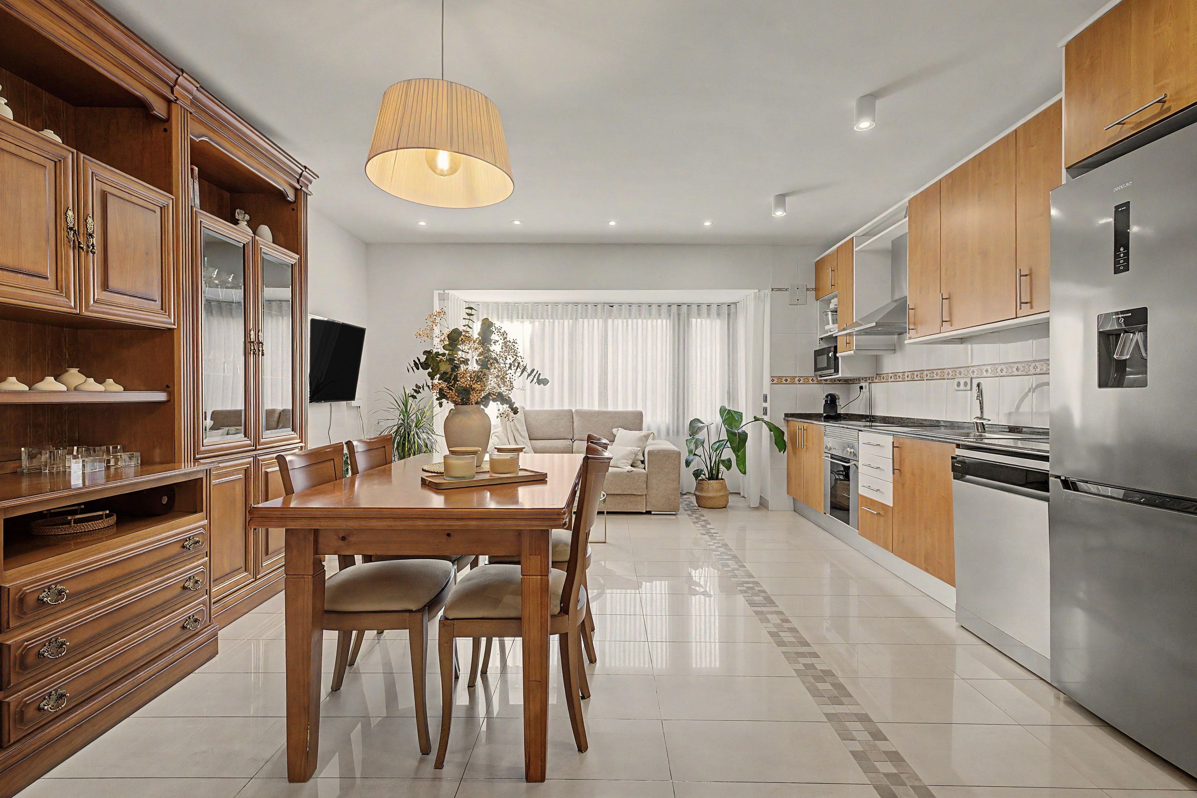 Een moderne keuken met een eethoek, houten kastjes, een roestvrijstalen koelkast en een eettafel met stoelen.