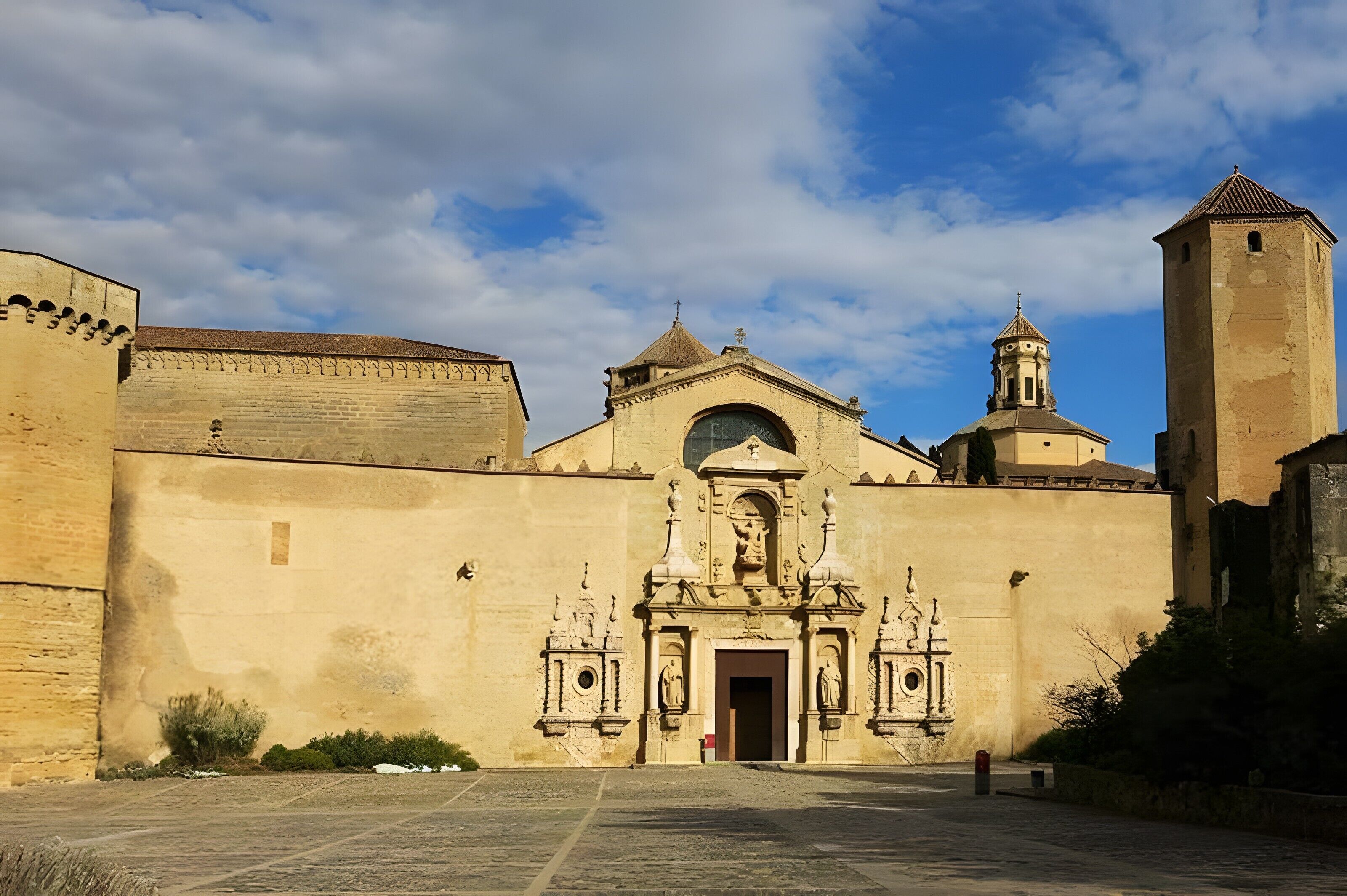 Un edificio histórico con una entrada central, una torre de campanas y un muro fortificado.