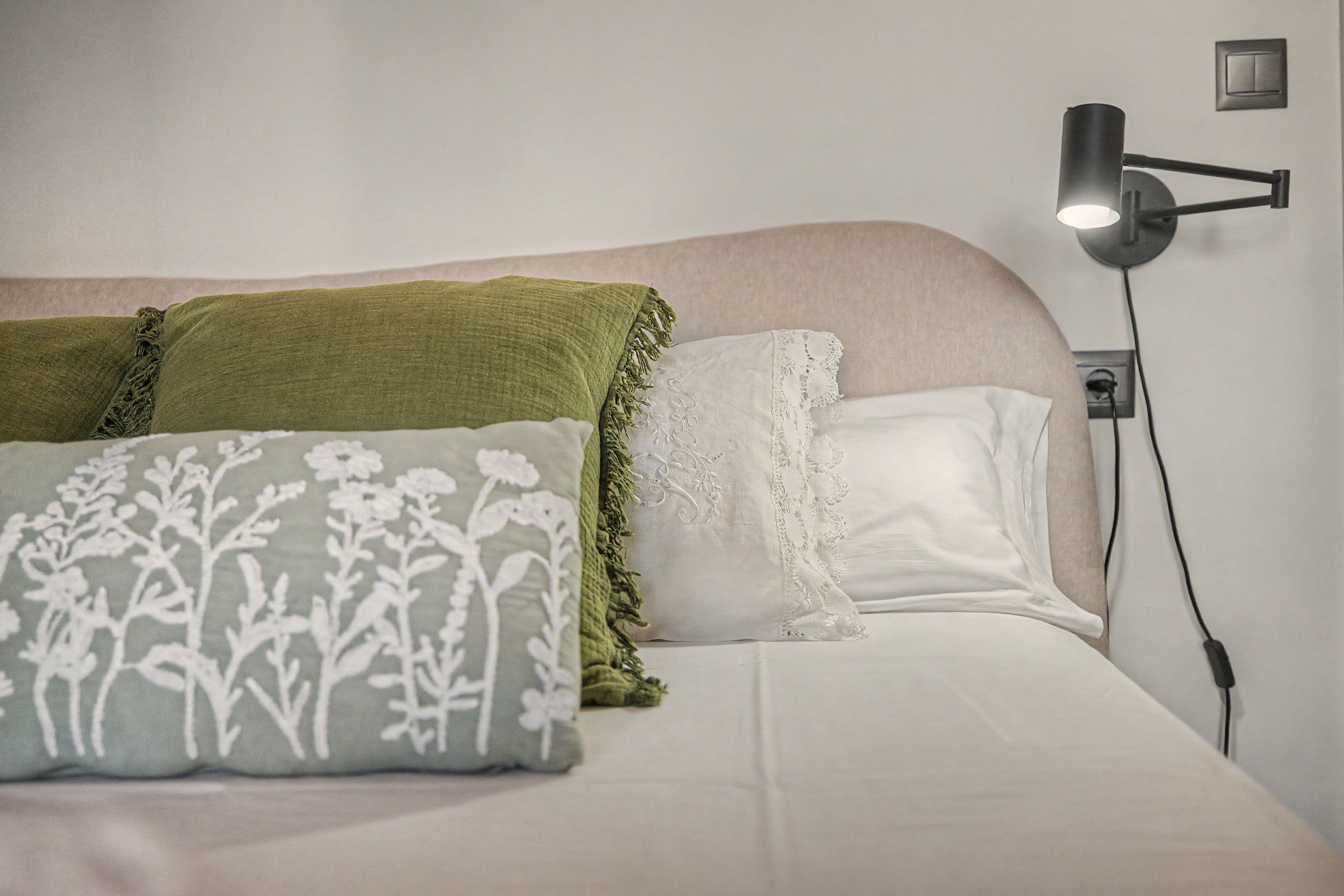 Un lit avec un matelas blanc, une couverture verte et deux oreillers ornés de motifs floraux et de dentelle.