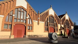 En bygning med buede vinduer og en rød dør, en stor stenskulptur i forgrunden, og en klar blå himmel.