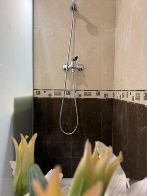 Eine Dusche mit Handbrause, Wandarmatur und gefliestem Duschbereich mit dekorativer Bordüre.