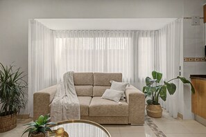 A living room with a beige sofa, a coffee table, and two potted plants. - Apartment 'Rural Ca La Roser' with Private Terrace, Wi-Fi and Air Conditioning (L'Espluga de Francolí)