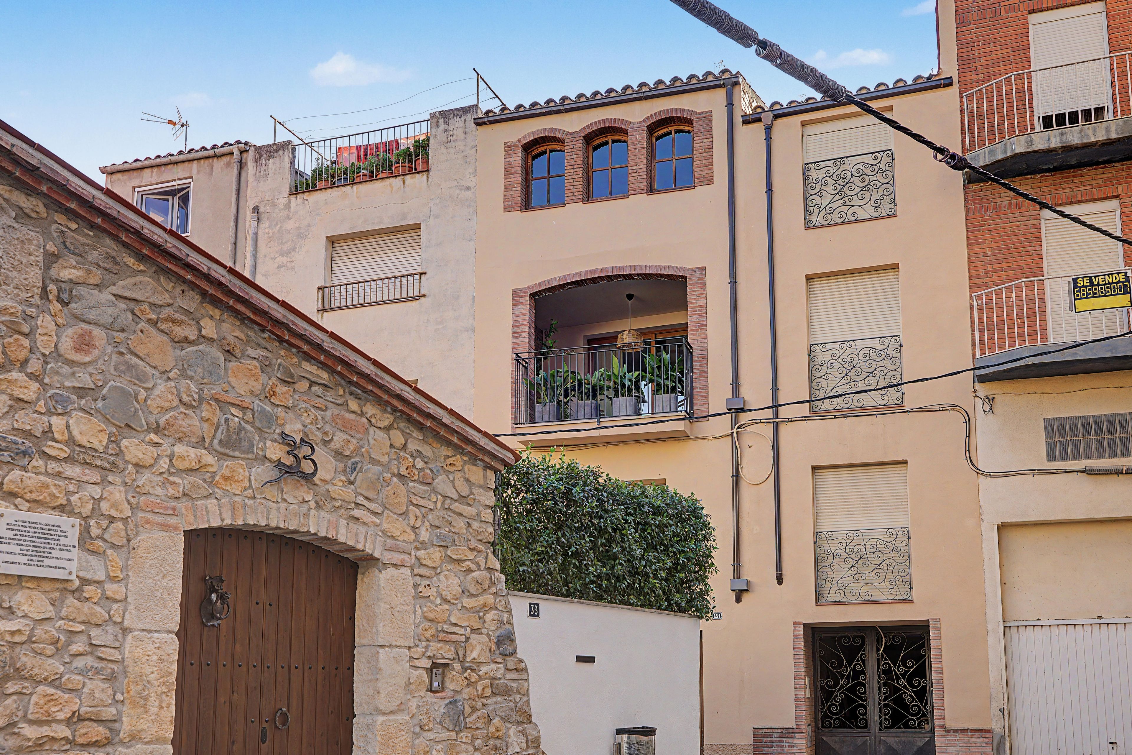 Edificio de piedra con puerta de madera, balcón con plantas y un letrero que indica ofertas.
