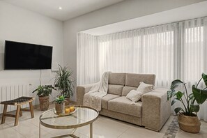 Una sala de estar moderna con un sofá color beige, una mesa de centro de vidrio y plantas en macetas.