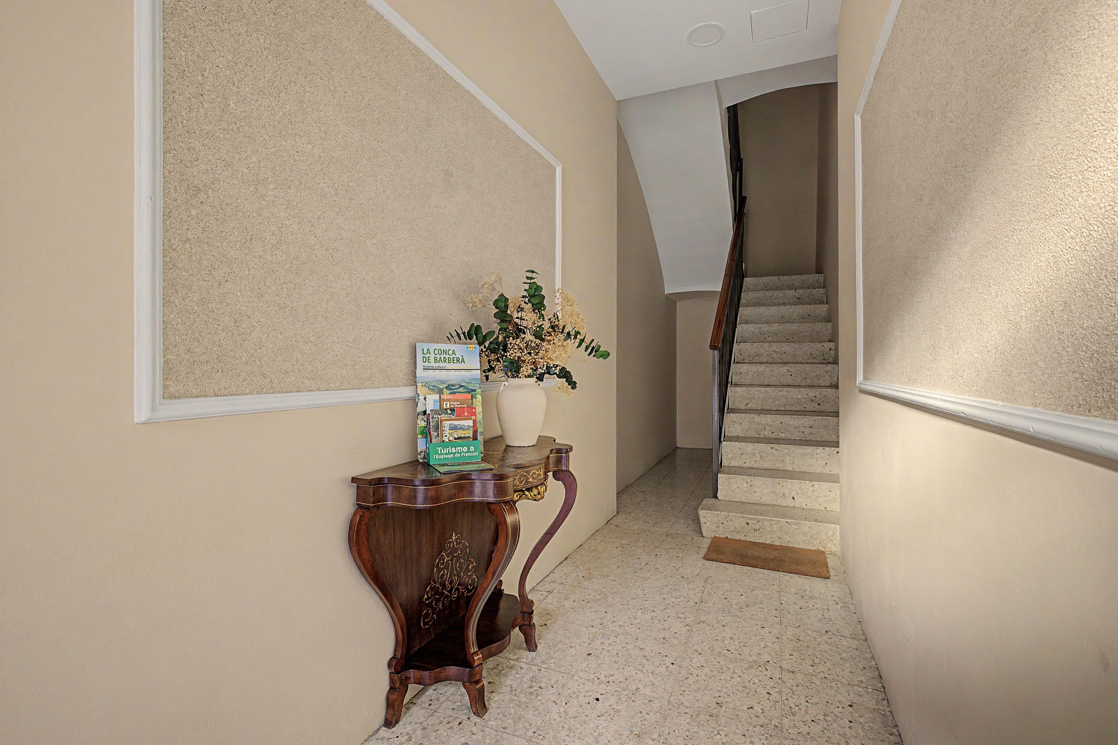 A hallway with a wooden console table, a vase with flowers, and a staircase leading to an upper floor.