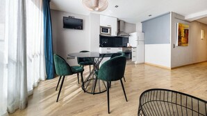 Eine moderne Küche mit Flachbildfernseher, einem Essbereich mit Glastisch und grünen Stühlen sowie einem Holzboden.