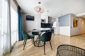 A modern kitchen with a flat-screen TV, a dining area with a glass table and green chairs, and a wooden floor. - Sicilia-1602 - Studio Apartment, Sleeps 2 (Barcelona)