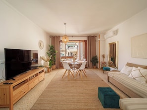 Ein Wohnzimmer mit Fernseher, Holzmöbeln, einem Esstisch und einem Sofa.