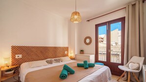 Ein Hotelzimmer mit einem Bett, einem Sessel, einem Fenster, einem an der Wand befestigten Spiegel und einem kleinen Tisch mit einer Pflanze.
