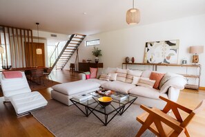 Een moderne woonkamer met een bank, een voetenbankje, een salontafel en een trap.