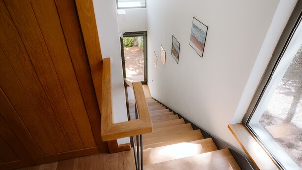 Una escalera de madera con barandilla que conduce a una habitación con ventana y cuadros en la pared.