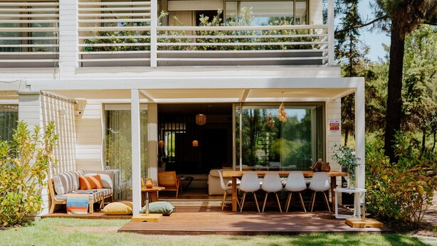 Ein modernes, zweistöckiges Haus mit Terrasse, Außenmöbeln und einem Balkon.