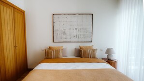 Un dormitorio con una cama grande, un armario de madera, una obra de arte en la pared y una lámpara de noche.