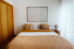 Un dormitorio con una cama grande, un armario de madera, una obra de arte en la pared y una lámpara de noche.