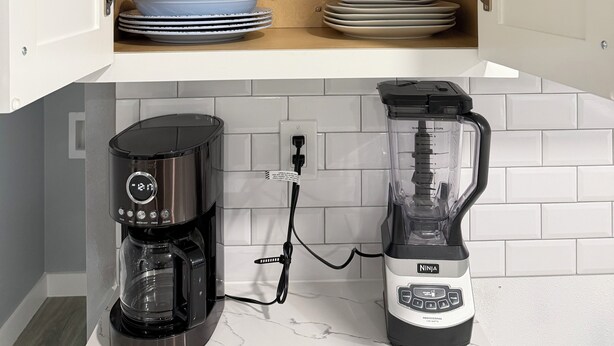 Una cocina con cafetera, licuadora y repisas con platos y tazones.