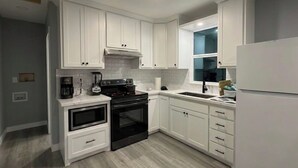 Una cocina con armarios blancos, una estufa negra y un refrigerador blanco.