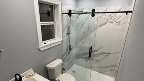 Un baño moderno con cabina de ducha de vidrio, un inodoro blanco y un lavabo con espejo.