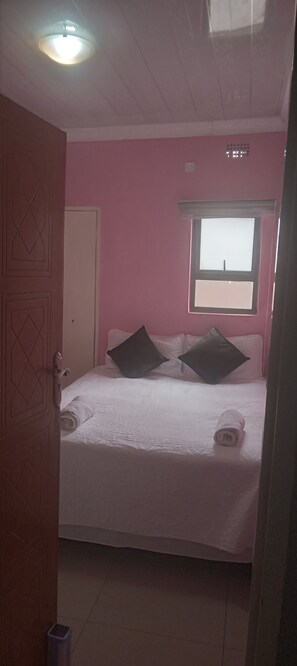 Ein Schlafzimmer mit Bett, Kissen, einem Fenster und einer Tür.